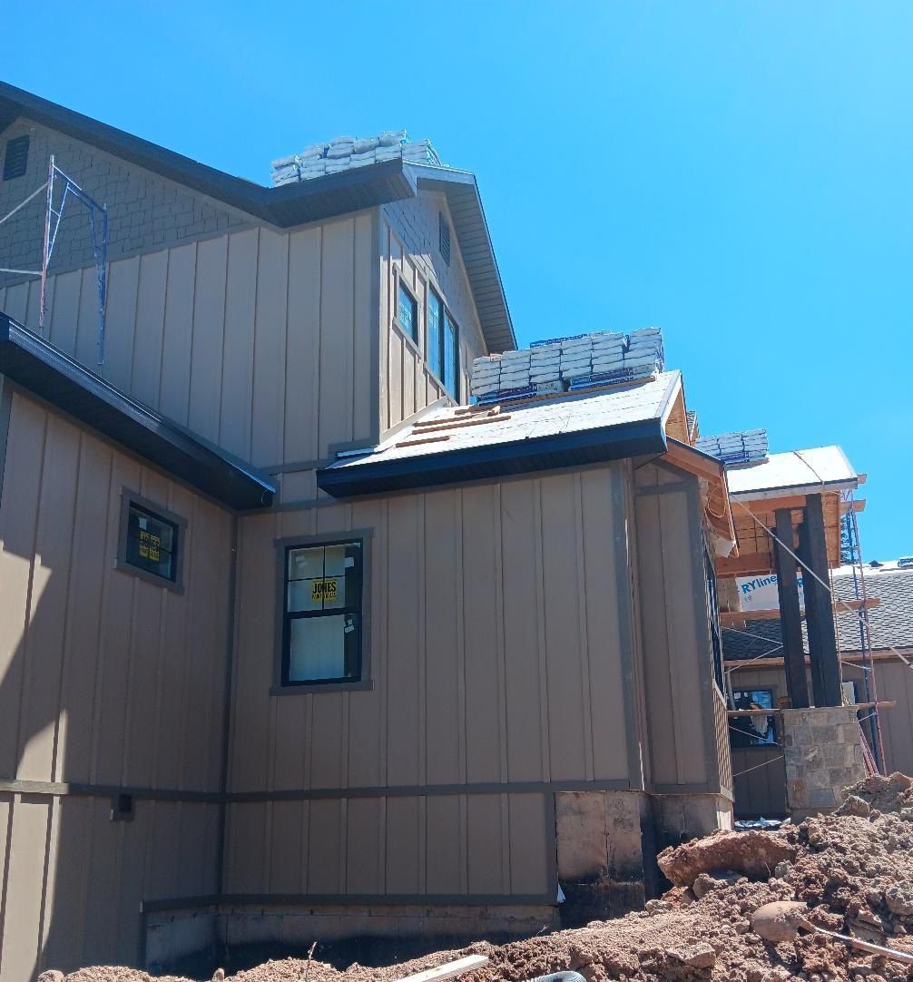 Exterior of a house under construction; beige siding, blue sky, roof framing visible.