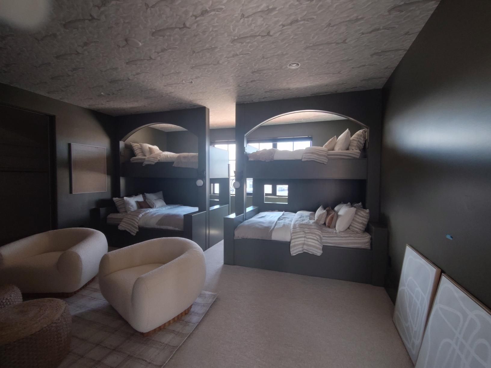Bedroom with bunk beds, two armchairs, and art. Dark walls, neutral bedding, and white accents.