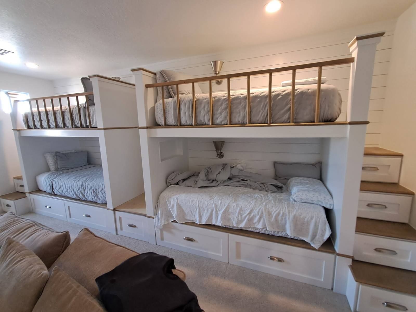 Built-in bunk beds with white cabinets, drawers, and wooden accents. Beds are made with gray and white linens.