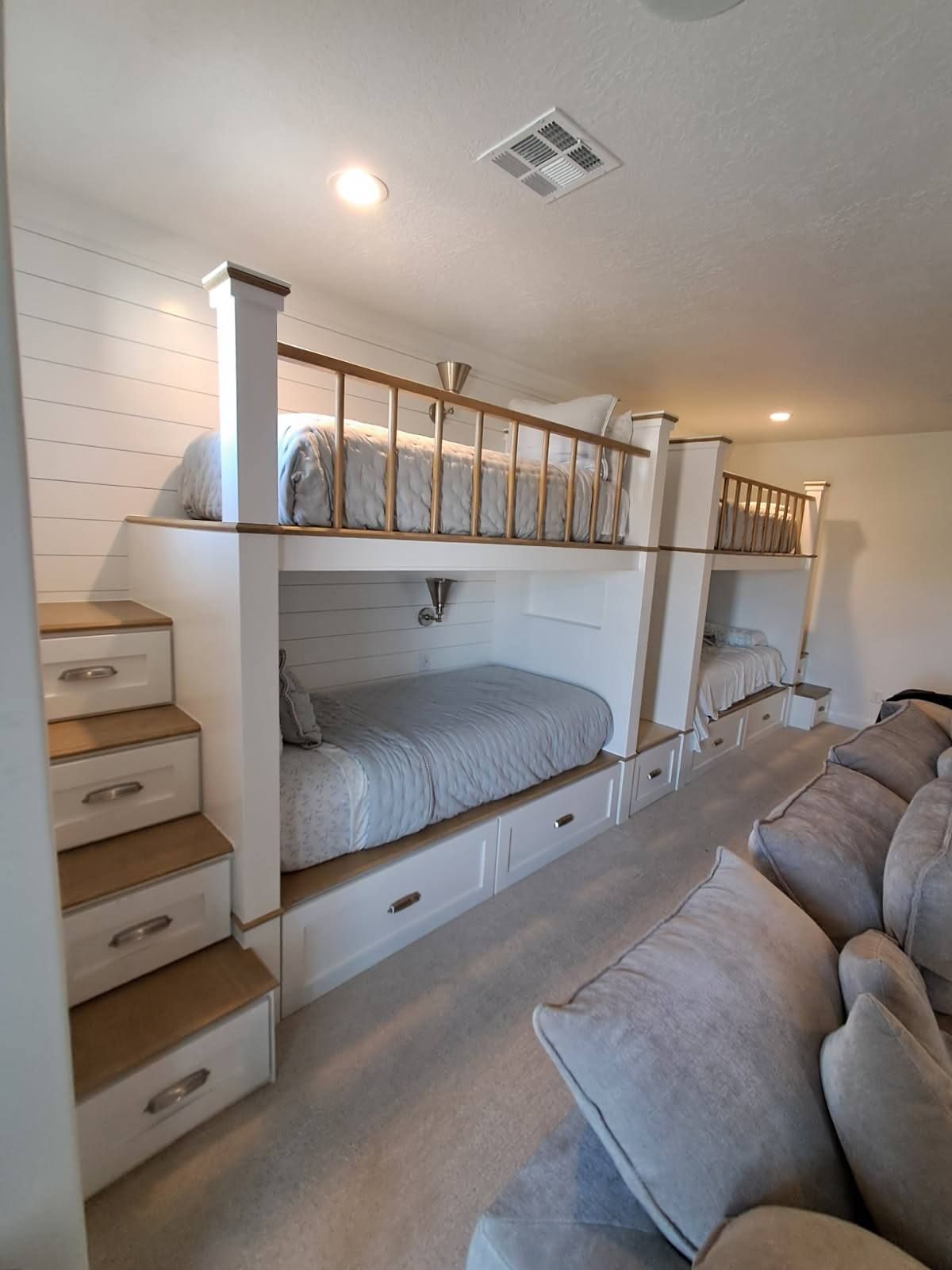 Built-in bunk beds with storage drawers and stairs, next to a gray couch, in a room with white walls.