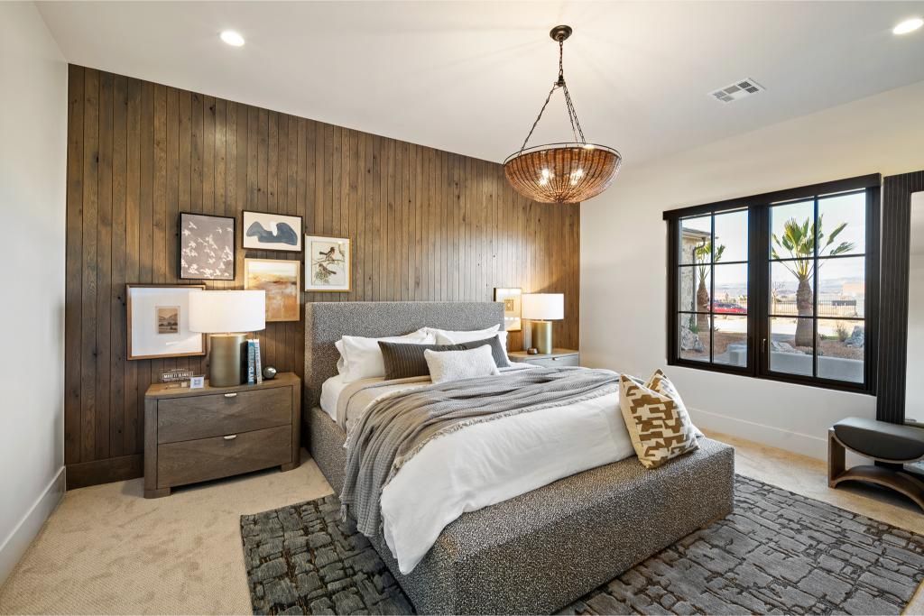 Bedroom with wood accent wall, bed, nightstand, art, rug, and window.