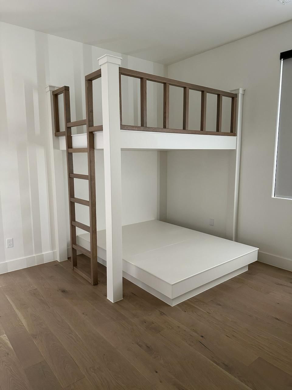 Built-in bunk beds with storage drawers and stairs, next to a gray couch, in a room with white walls.