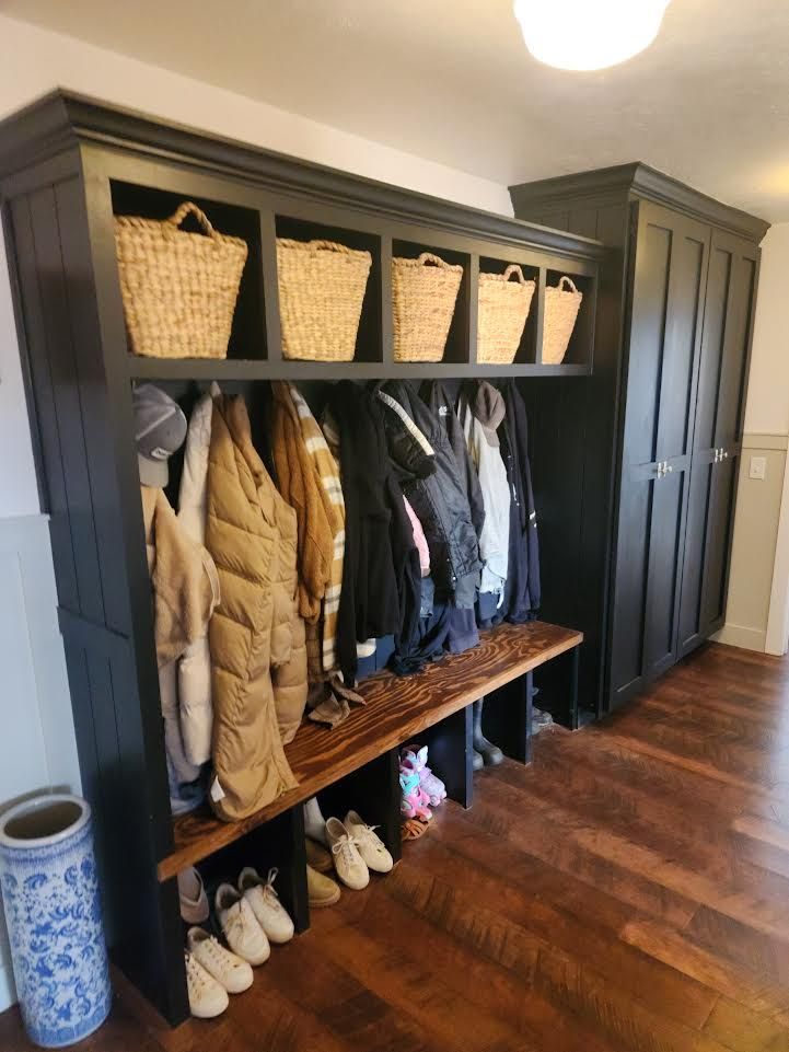 Built-in mudroom cubbies with woven baskets, coats, boots, and a bench beside a dark cabinet
