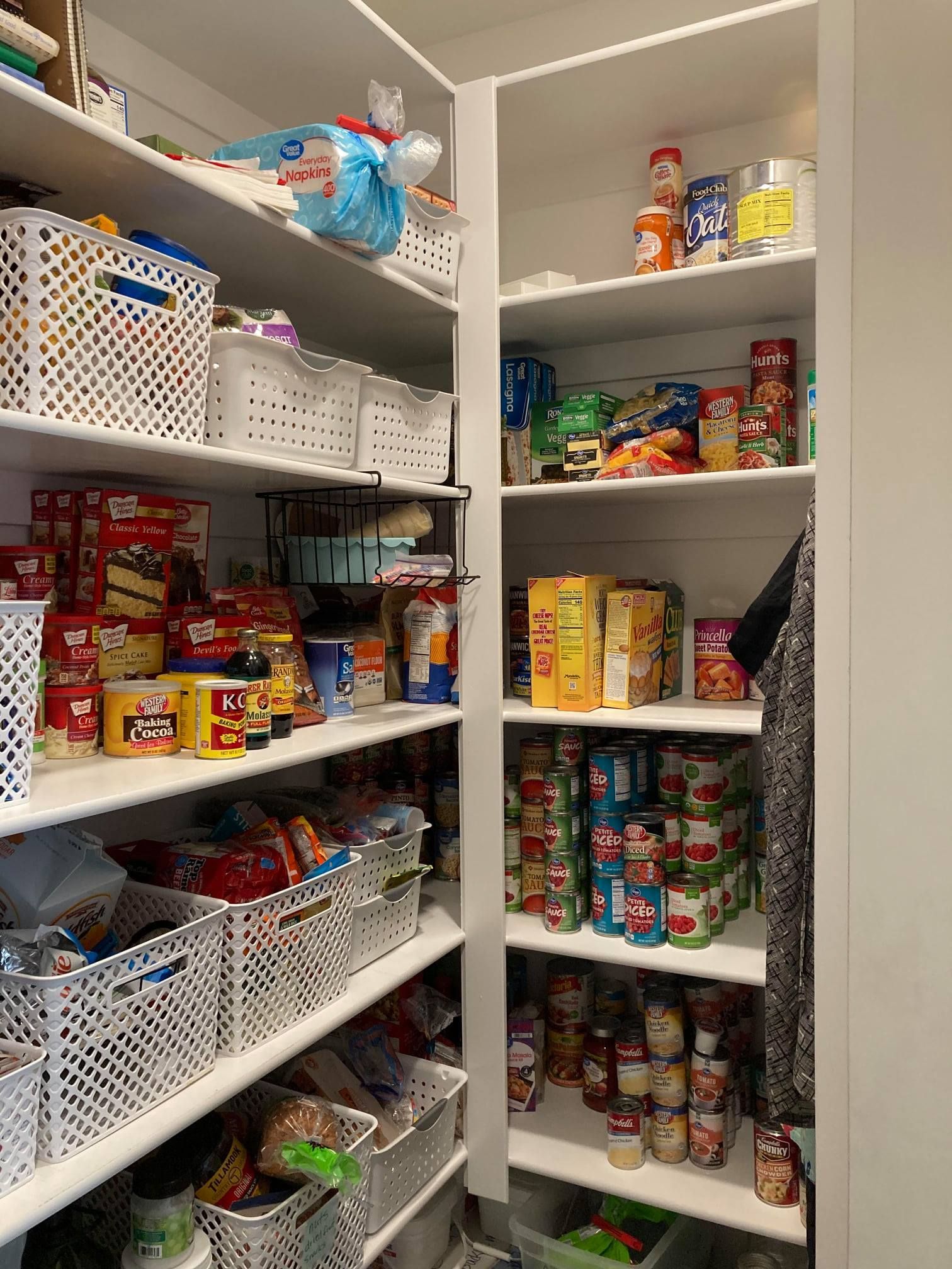 Walk-in pantry stocked with canned goods, jars, snacks, and pantry baskets on white shelves