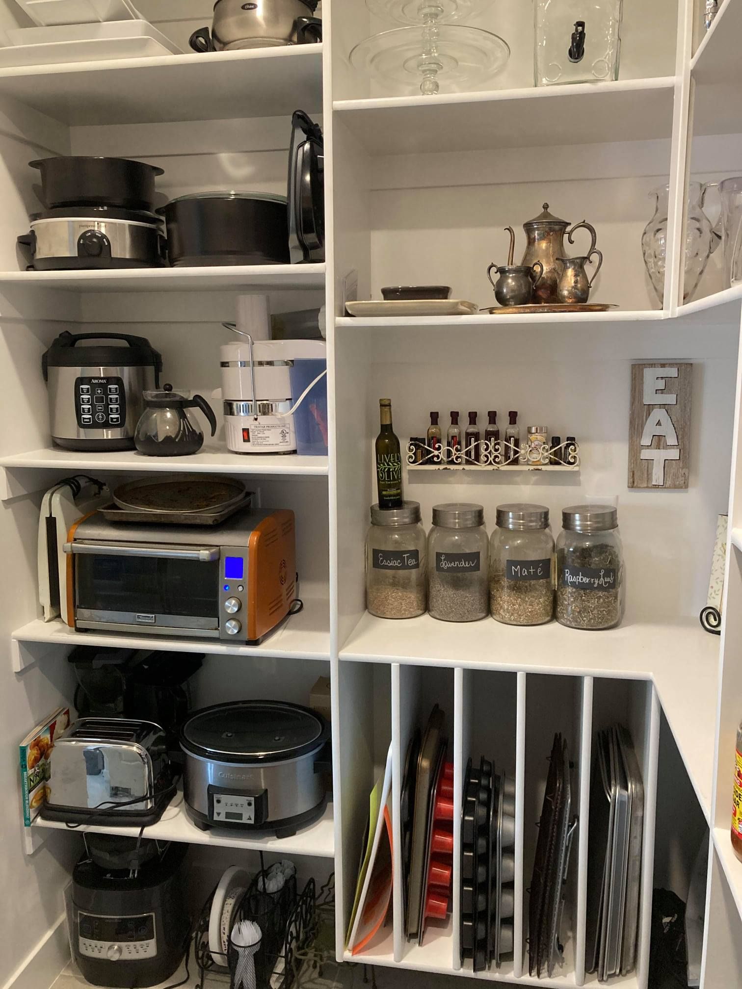 White pantry shelves stocked with small appliances, jars, spices, a tea set, and recipe binders