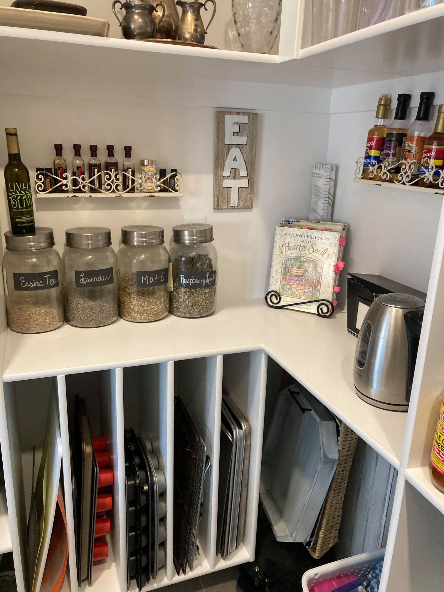 Pantry shelf with jars, bottles, cookbooks, and a small “EAT” sign above cubbies.