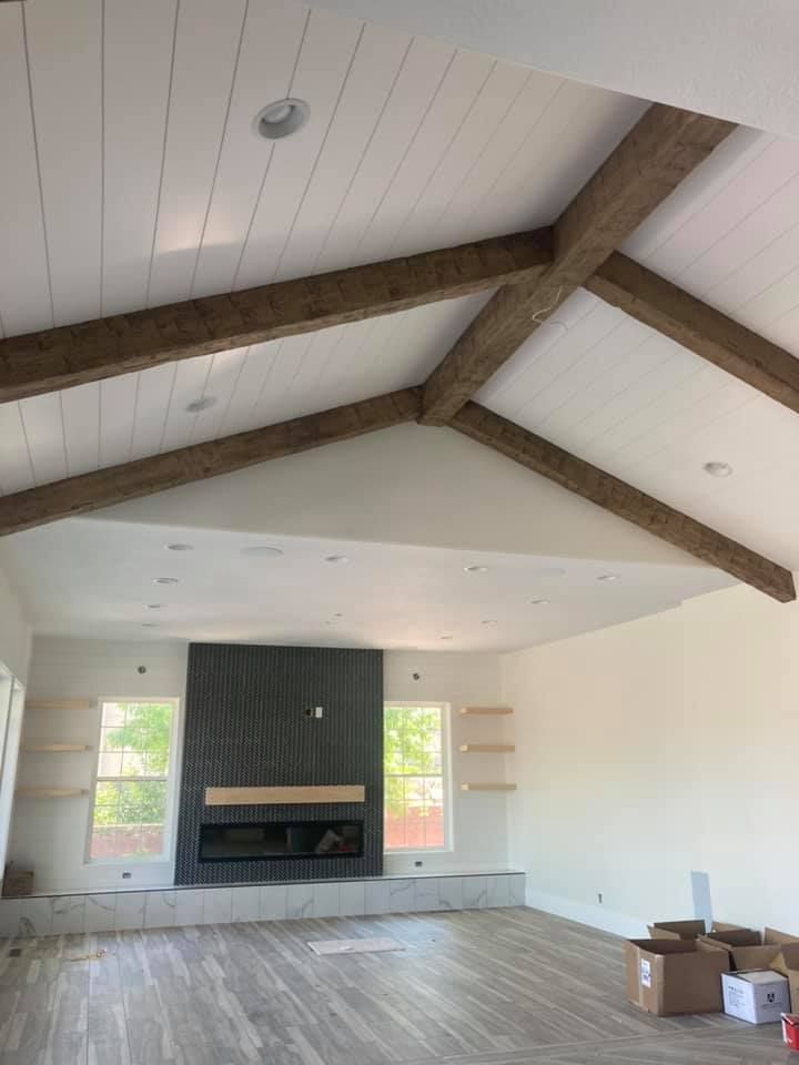 Empty living room with vaulted ceiling, exposed beams, fireplace, and boxes on the floor