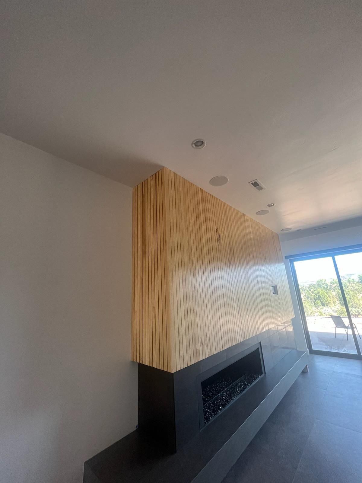 Modern living room with a wood-paneled fireplace wall and large window overlooking outdoors