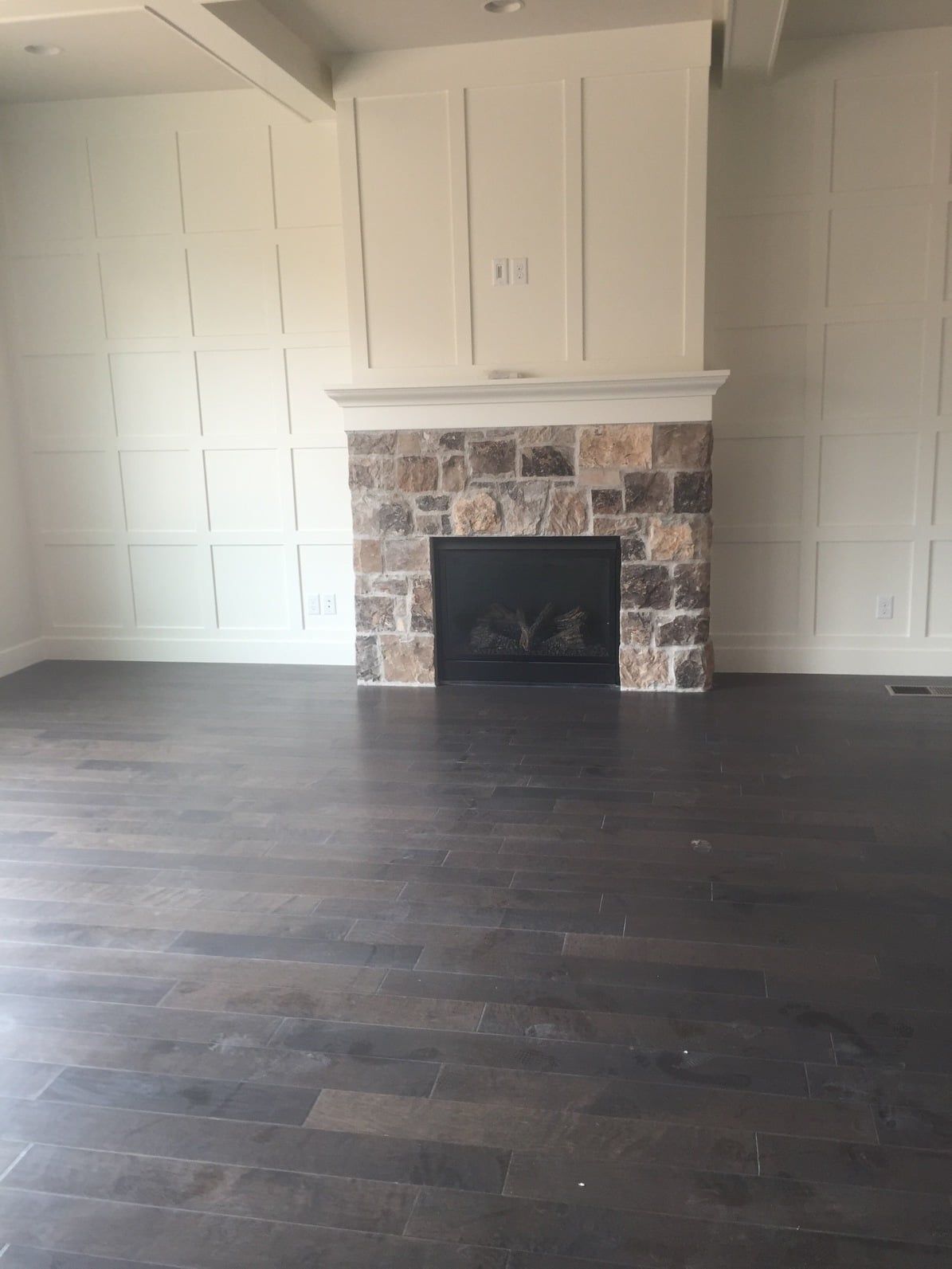Empty living room with dark wood floor, white built-in cabinets, and a stone fireplace mantel.