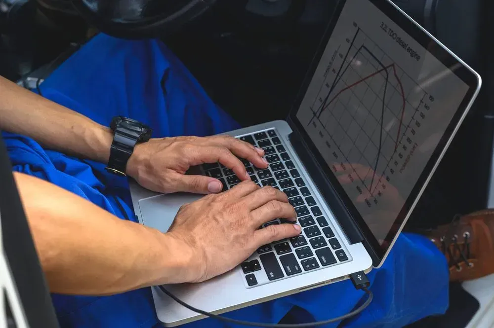 Person in Blue Overalls Using Laptop in a Vehicle, Analyzing Graphs — Advanced Auto Electrics & Mechanical in Innisfail, QLD