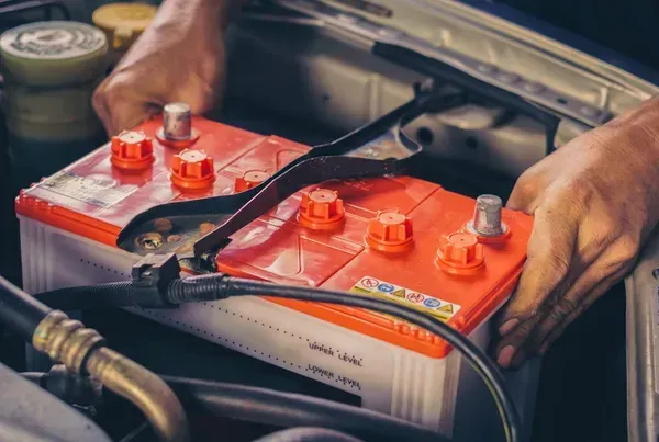 Hands Installing a Red Car Battery in the Engine Bay — Advanced Auto Electrics & Mechanical in Innisfail, QLD