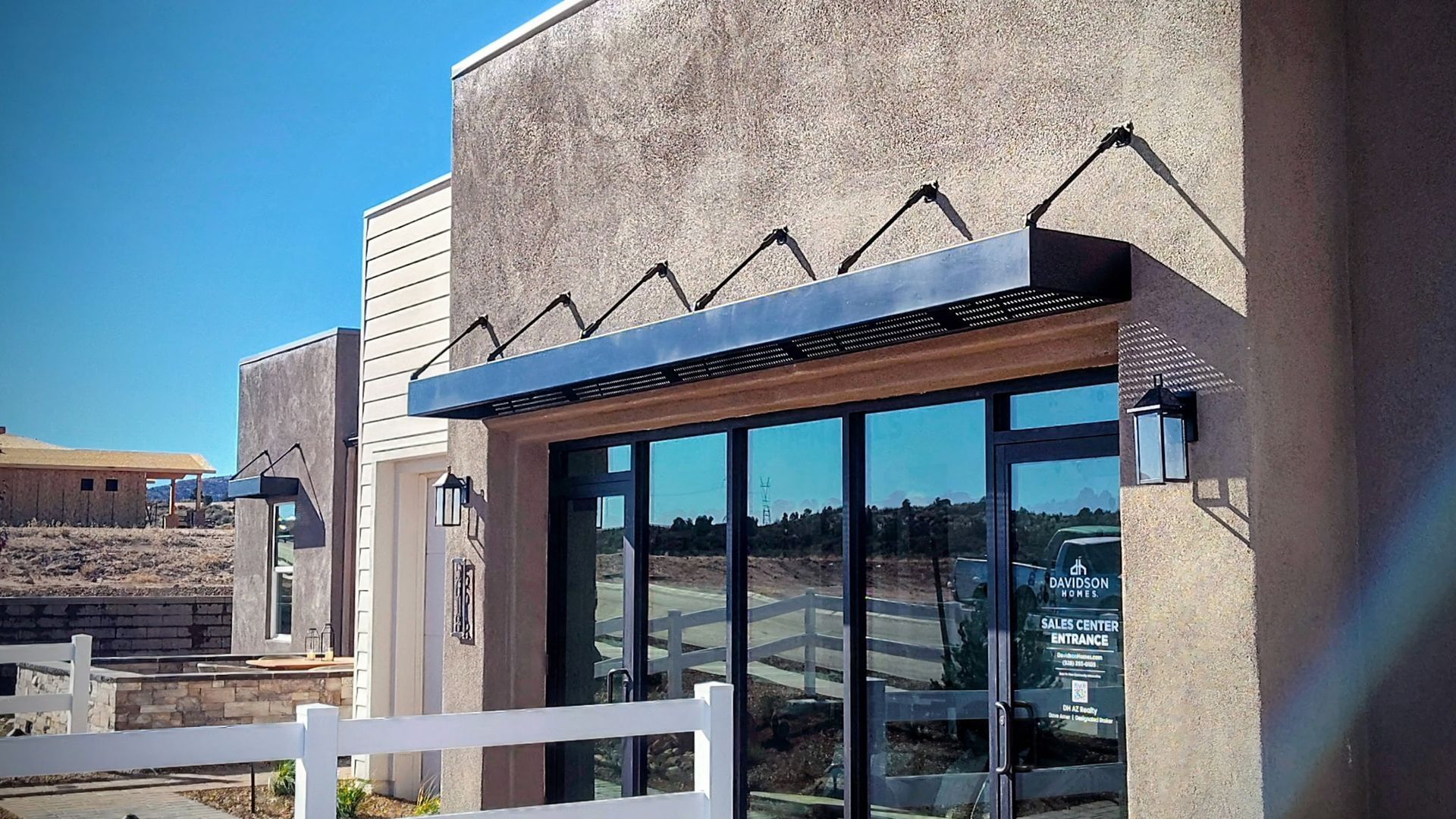 Exterior view of a building with a dark awning above a glass door and window. Sunny day.