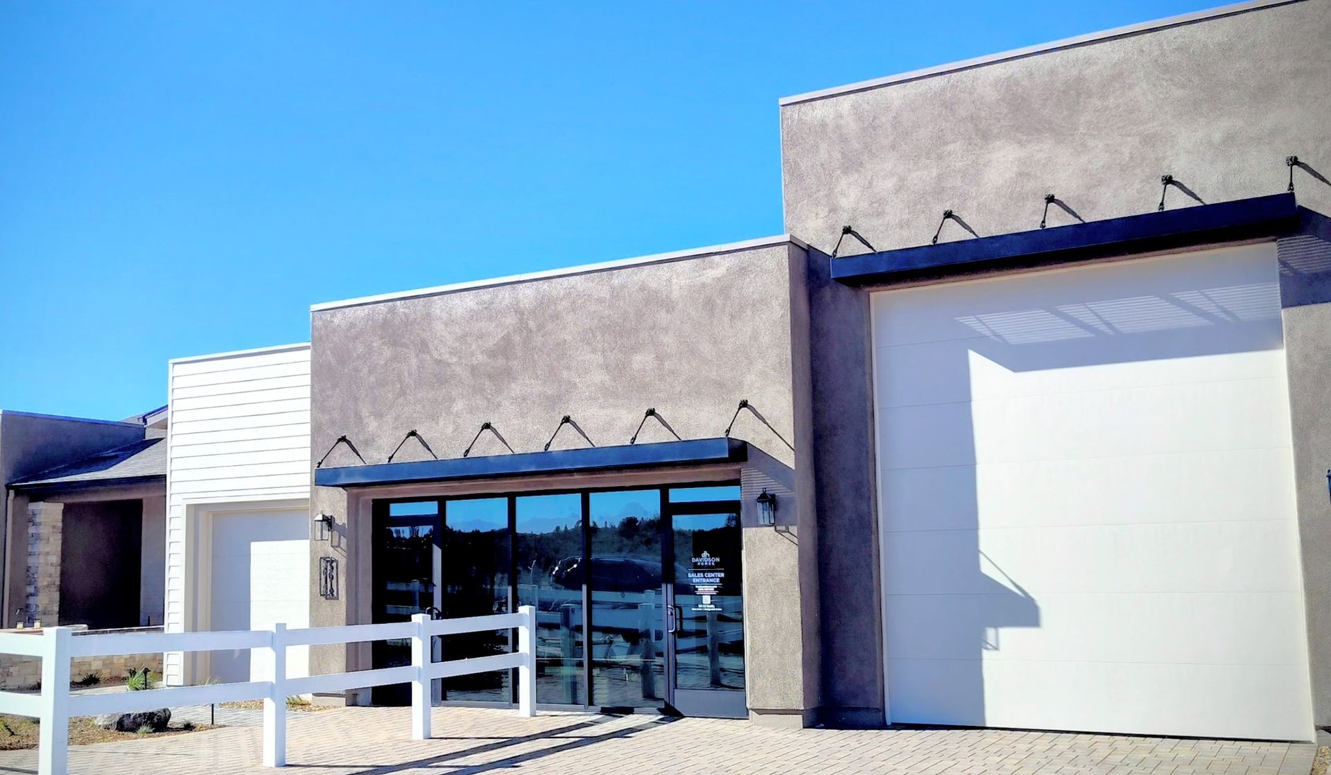 Modern building exterior with stucco walls, glass entrance, and awning under a bright blue sky.