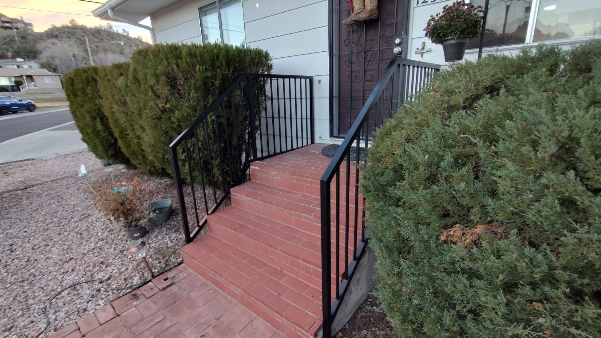 Exterior view of a house's entryway with steps, railing, and shrubs.