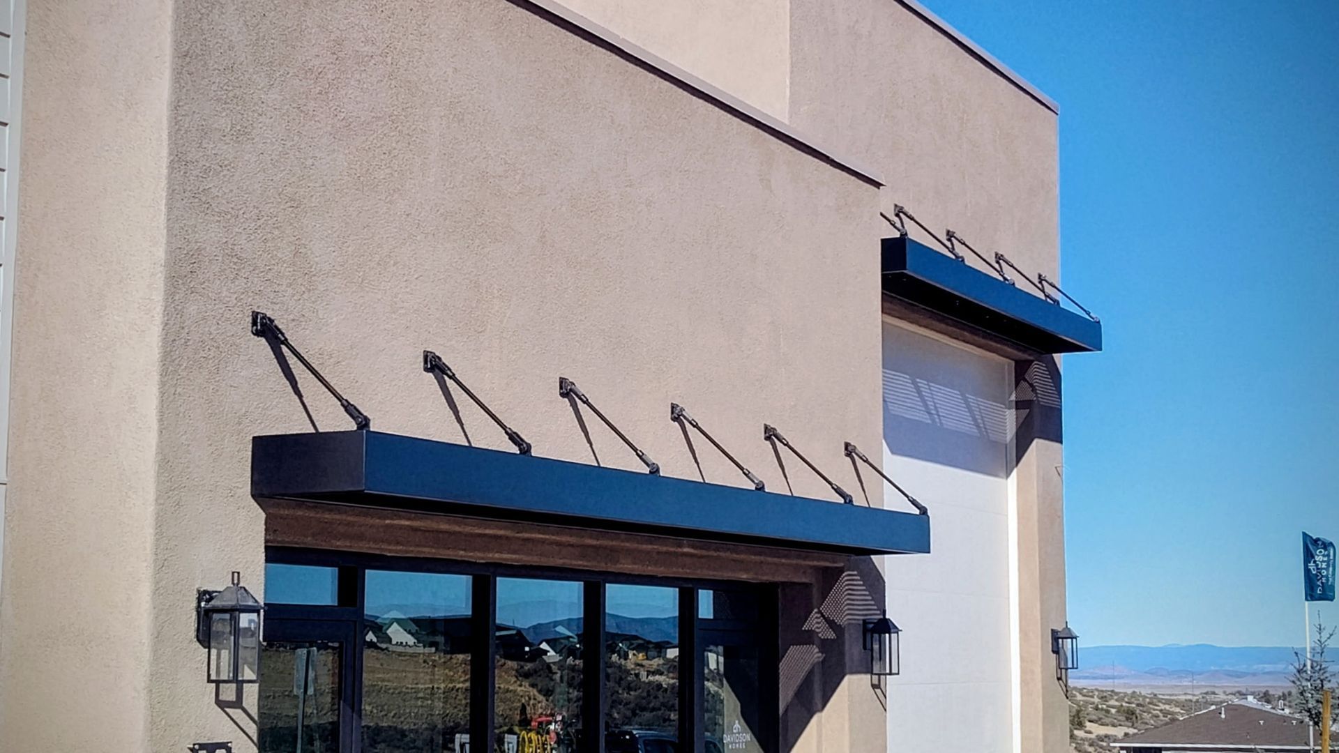 Building exterior with tan stucco and black awnings over windows.