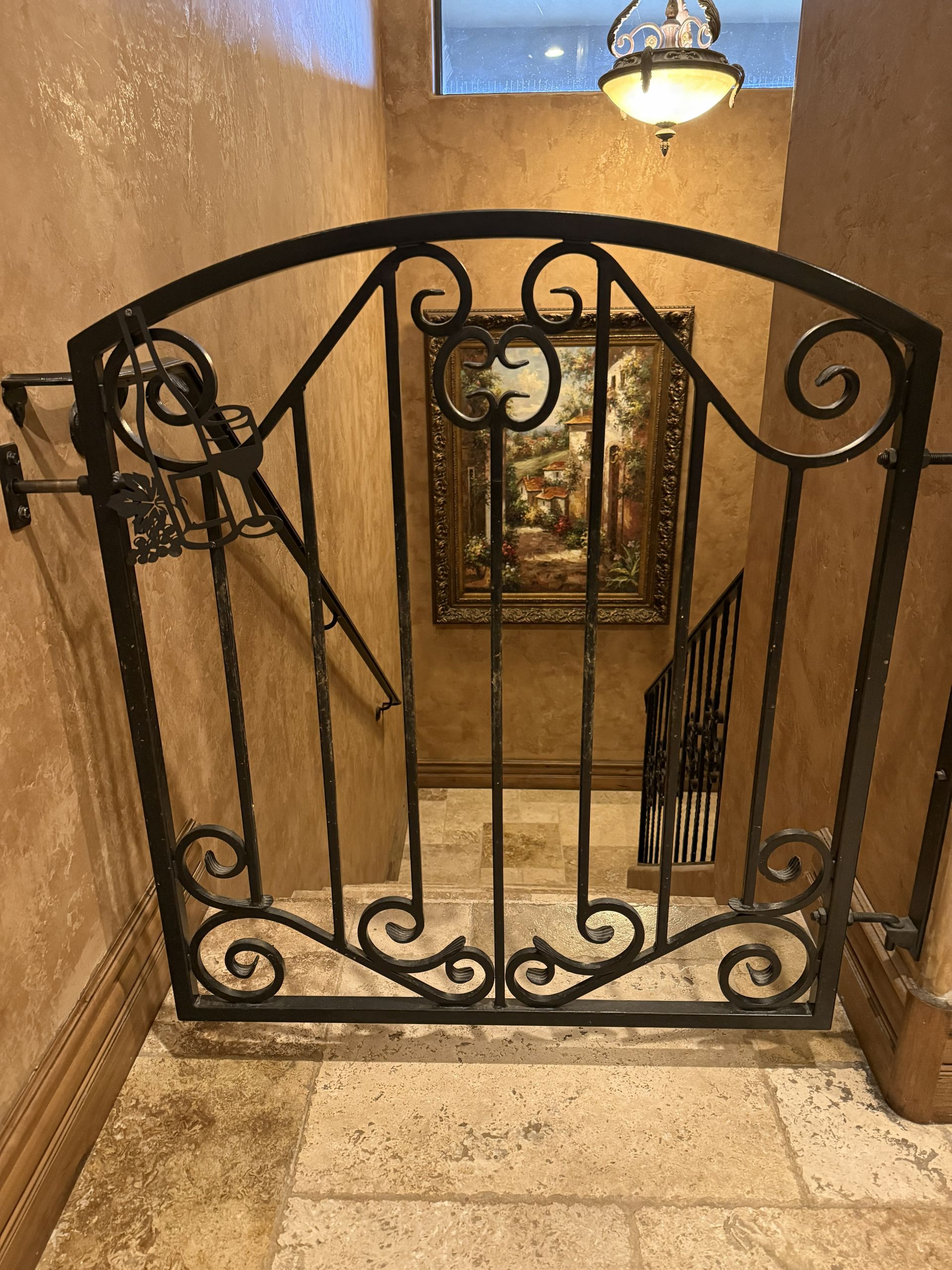 A decorative wrought-iron safety gate with scrollwork at the top of a stone-tiled staircase.