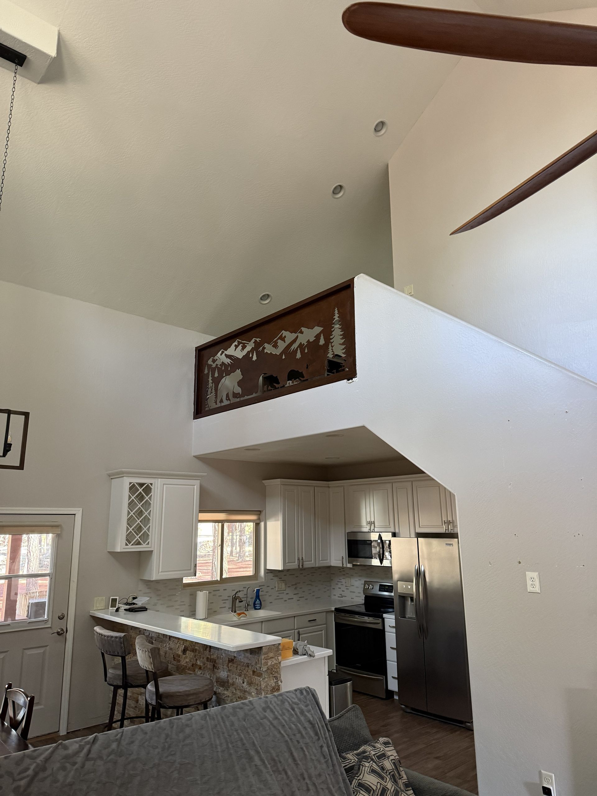 A kitchen with white cabinets, stainless steel appliances, and a breakfast bar, under a loft with decorative wood trim.