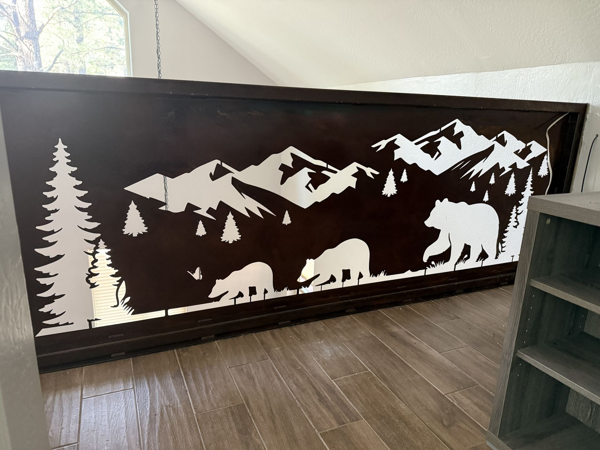 A decorative metal railing panel featuring a dark brown mountain landscape silhouette with white bears and evergreen trees.