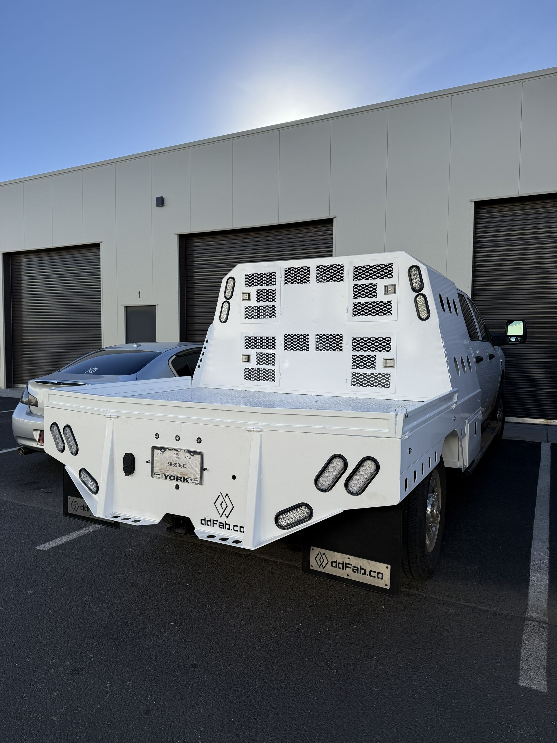 A white flatbed truck parked in front of a warehouse building on a sunny day.