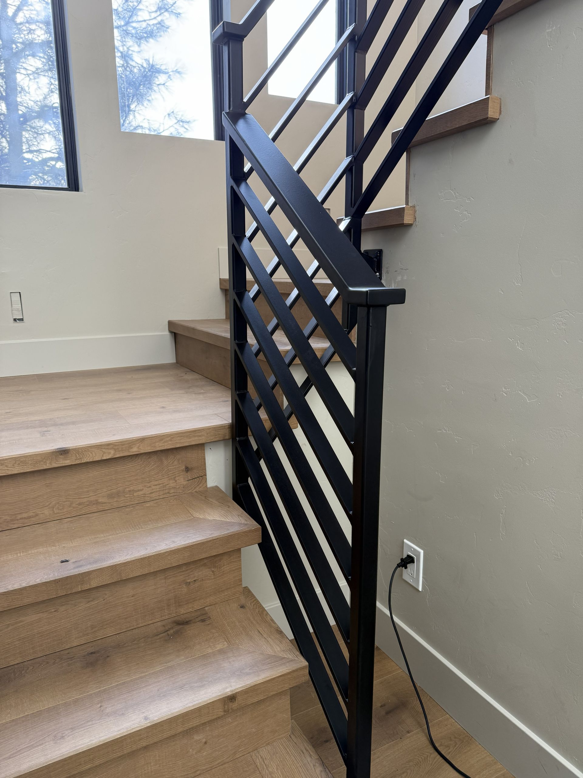 A staircase with light-colored wooden steps and a black metal railing featuring a diagonal lattice pattern.