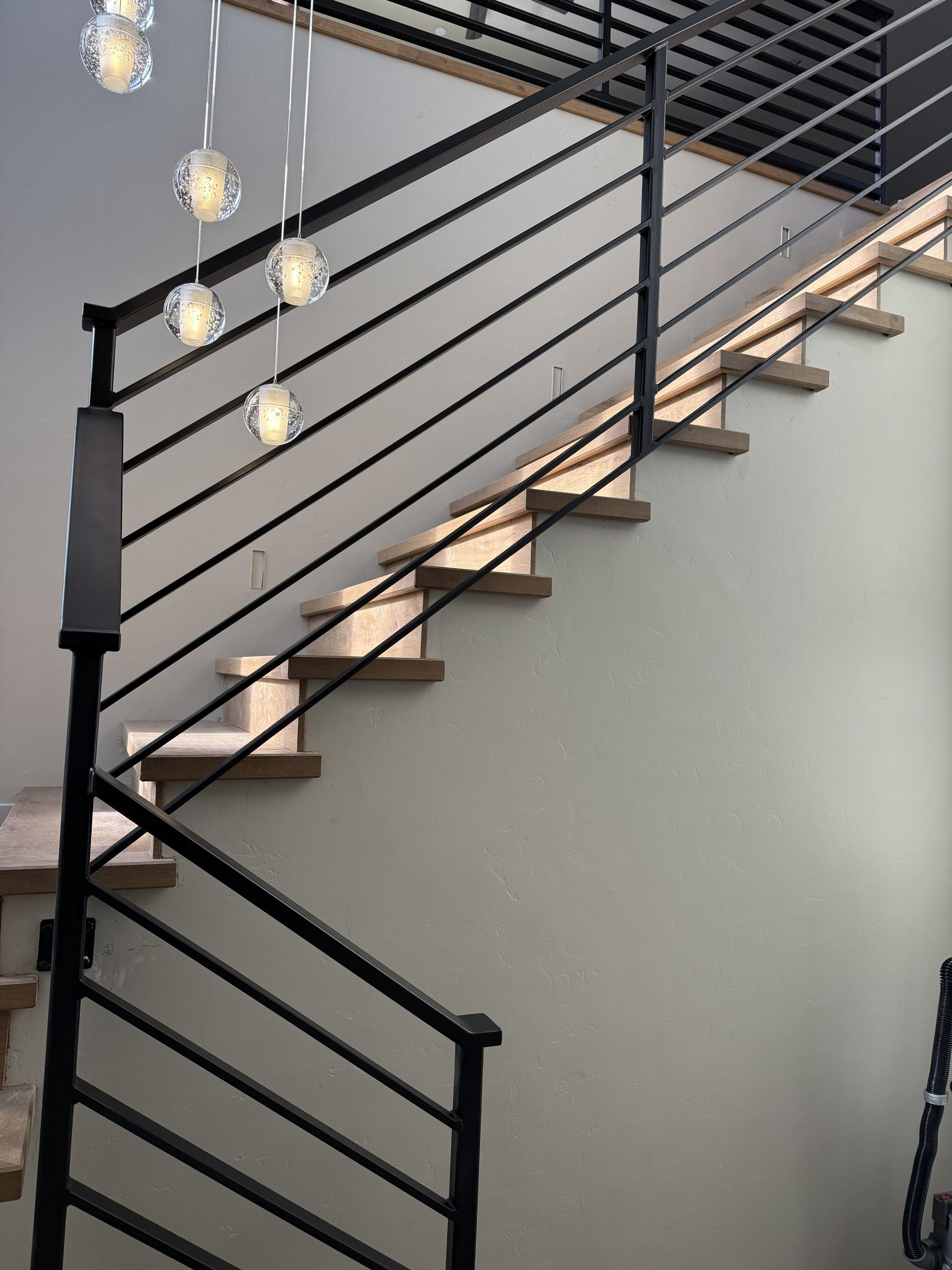 A staircase with wood steps, a black metal railing, and glowing pendant lights hanging above.
