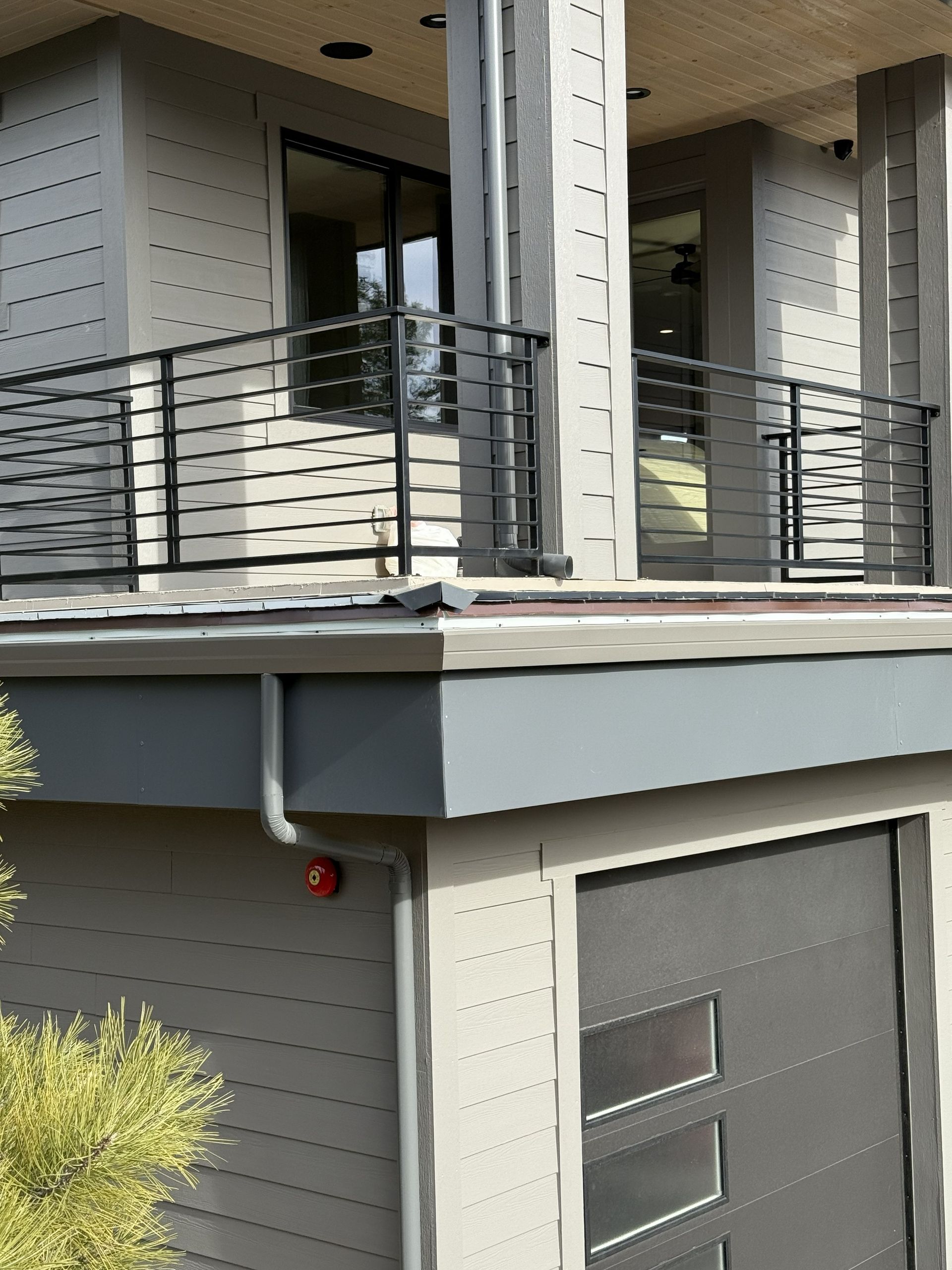 A modern two-story home with light grey siding, a black metal balcony railing, and a dark garage door with windows.
