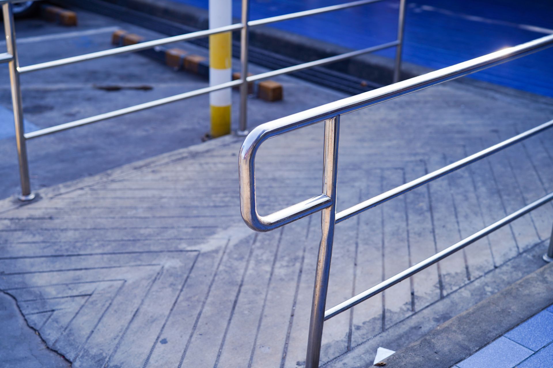 Concrete ramp with metal handrails, leading to a blue surface. A yellow and white pole is visible.