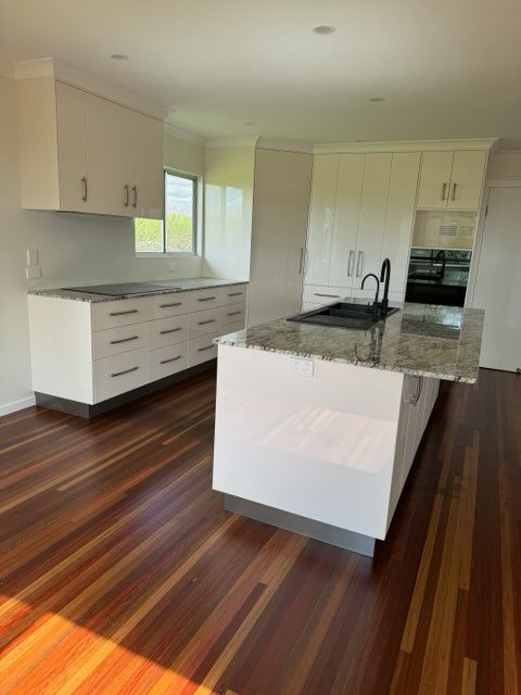 Modern White Kitchen With Granite Countertops, Island, and Dark Wood Floors — Red Emperor Constructions in Cannonvale, QLD