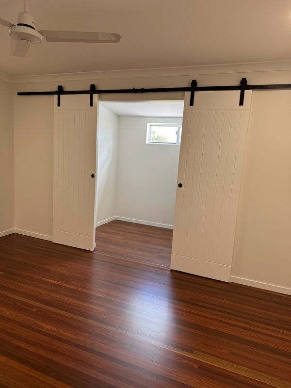Wooden Floor and White Walls With Two Sliding Barn Doors Leading to a Room — Red Emperor Constructions in Cannonvale, QLD