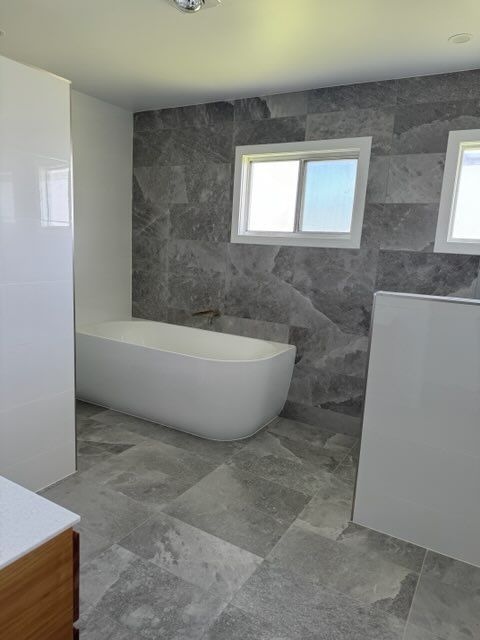 Freestanding White Bathtub Against a Grey Tiled Accent Wall — Red Emperor Constructions in Cannonvale, QLD