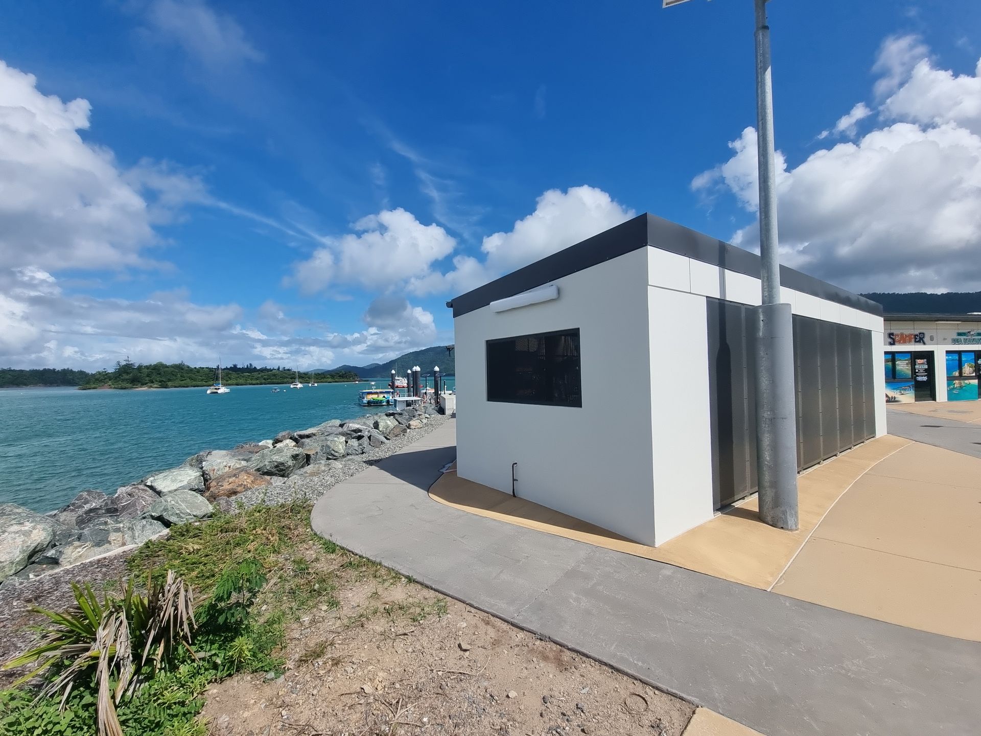 A small white building is sitting next to a body of water — Red Emperor Constructions in Cannonvale, QLD