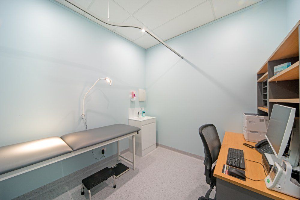 A doctor 's office with a bed , desk and computer — Red Emperor Constructions in Cannonvale, QLD