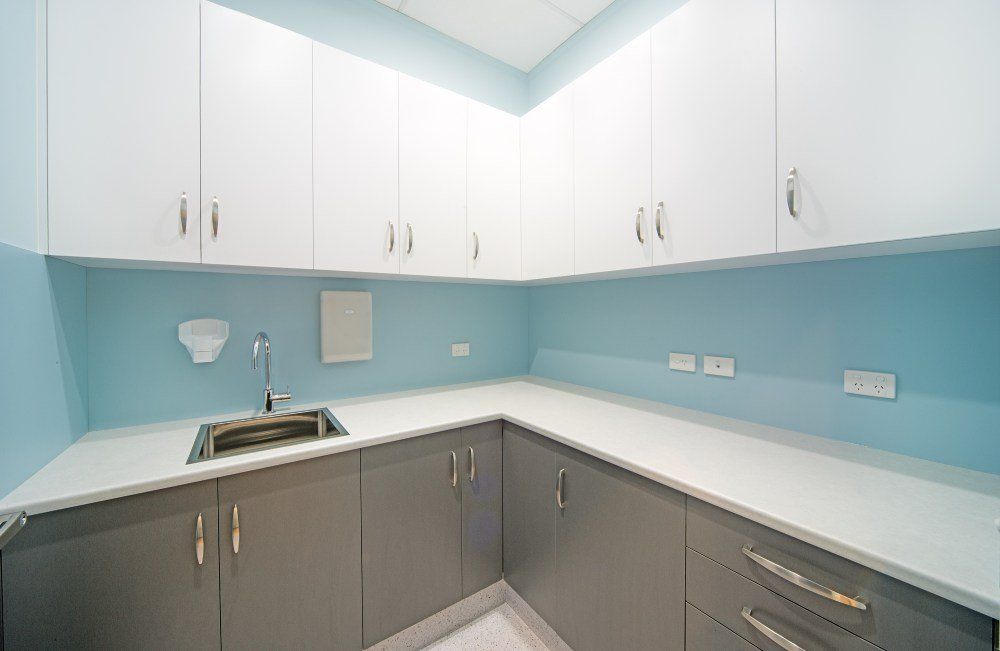 A kitchen with gray cabinets and white counter tops and a sink — Red Emperor Constructions in Cannonvale, QLD