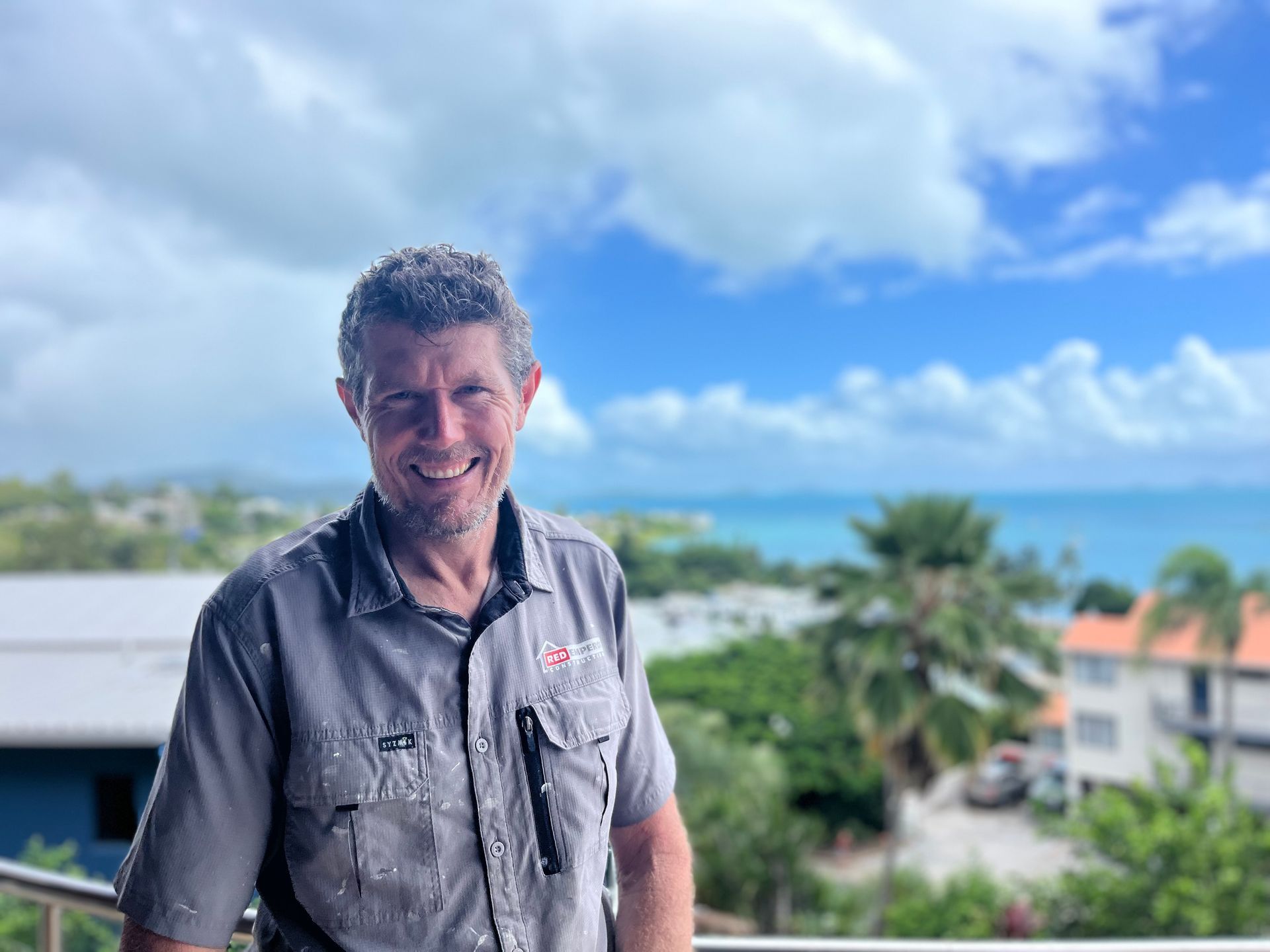 A man is standing on a balcony overlooking the ocean — Red Emperor Constructions in Cannonvale, QLD