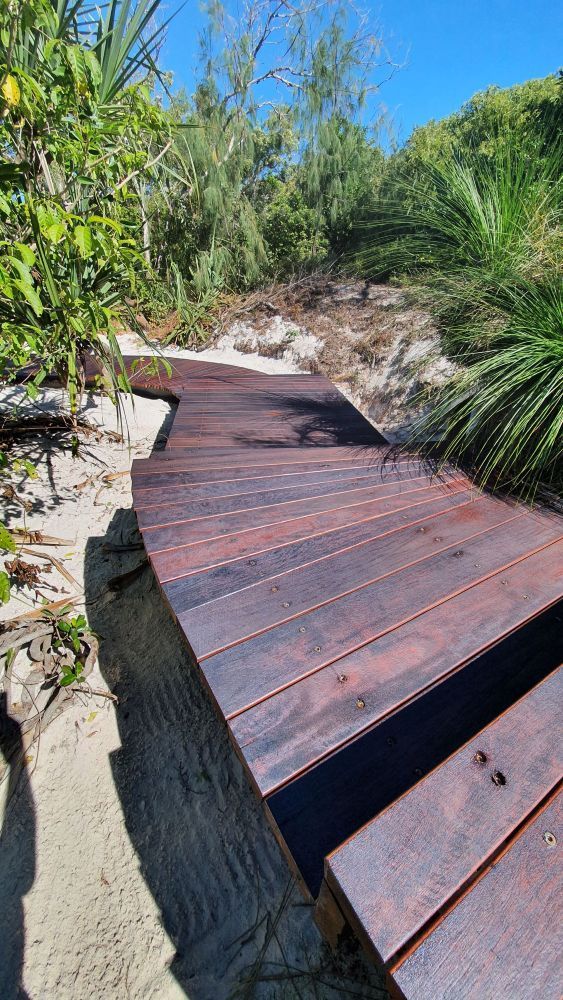 A Wooden Walkway Leading to a Beach Surrounded by Trees and Bushes — Red Emperor Constructions in Cannonvale, QLD