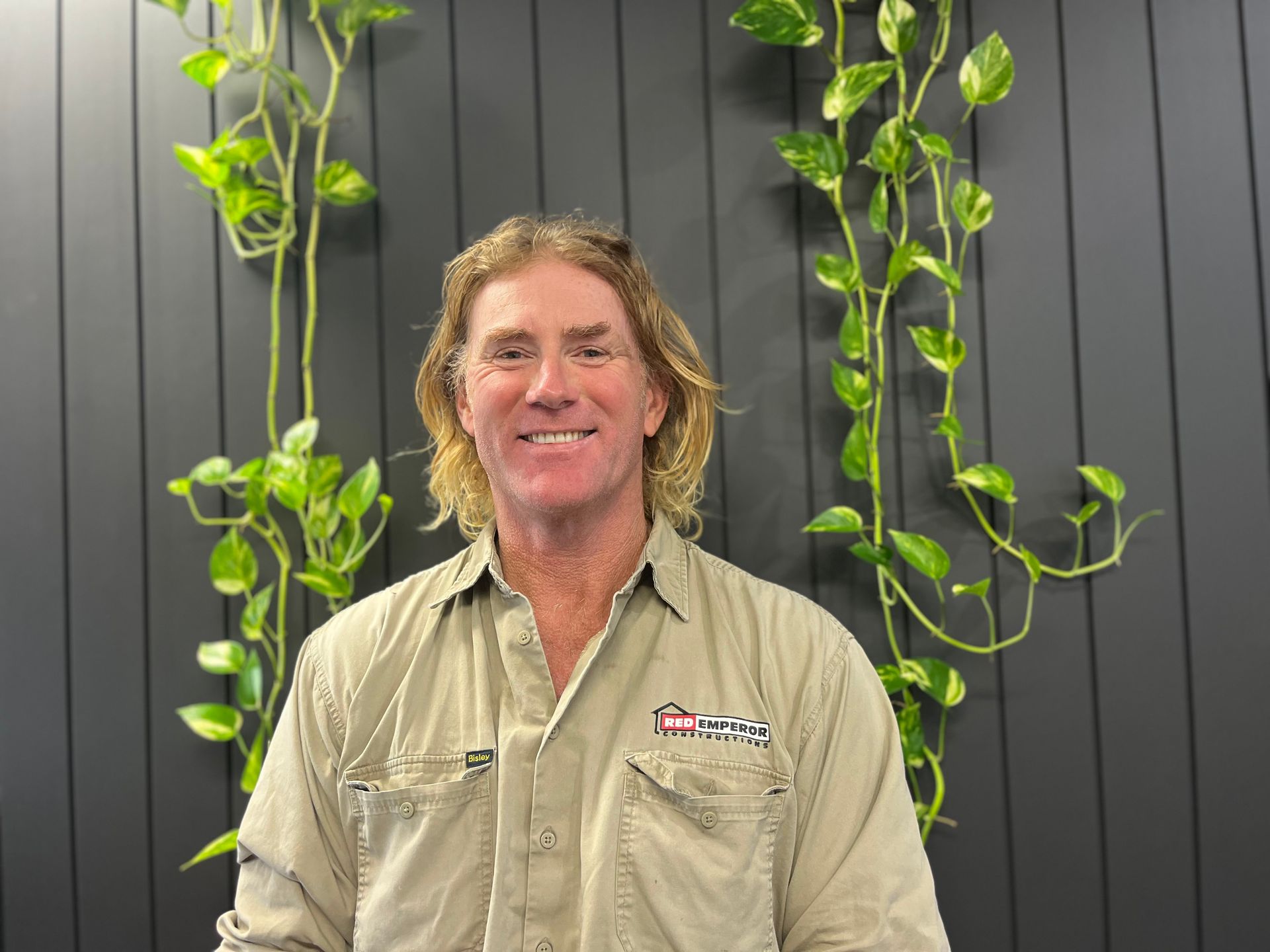 A man in a tan shirt is standing in front of a black wall — Red Emperor Constructions in Cannonvale, QLD