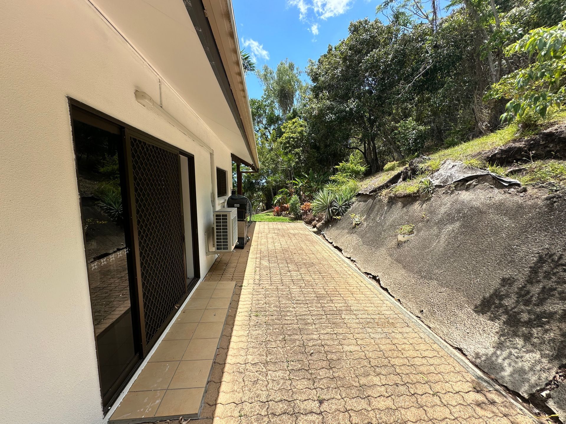 Sidewalk Next to a White Building With a Rock Retaining Wall and Lush Greenery — Red Emperor Constructions in Cannonvale, QLD