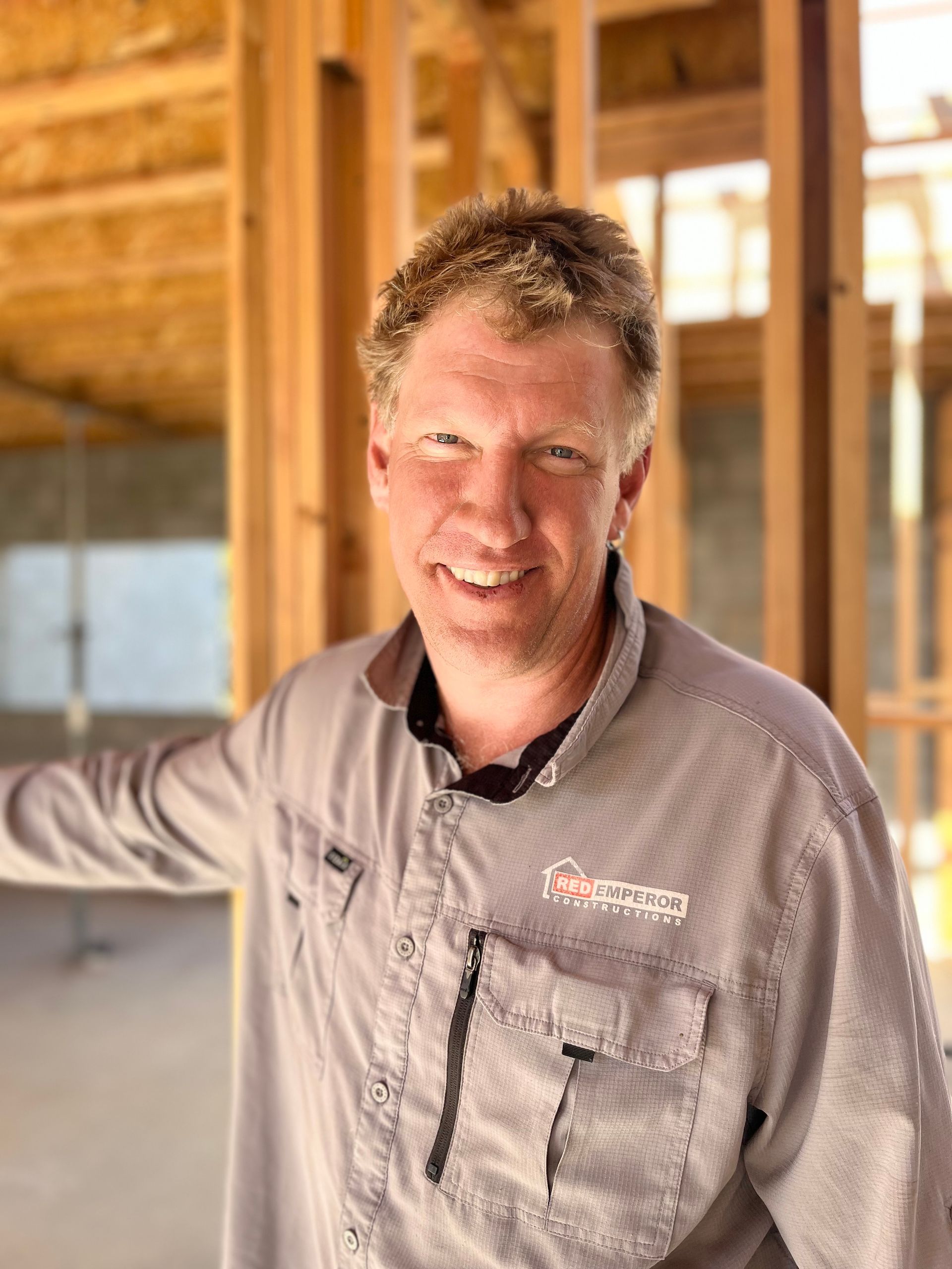 A man in a gray shirt is standing in front of a building under construction — Red Emperor Constructions in Cannonvale, QLD