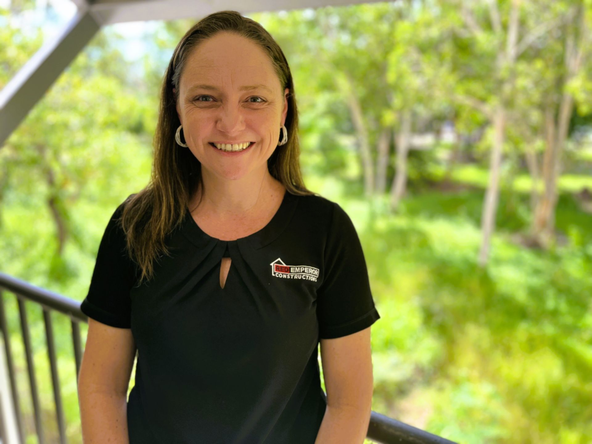 A woman in a black shirt is smiling and standing on a balcony — Red Emperor Constructions in Cannonvale, QLD