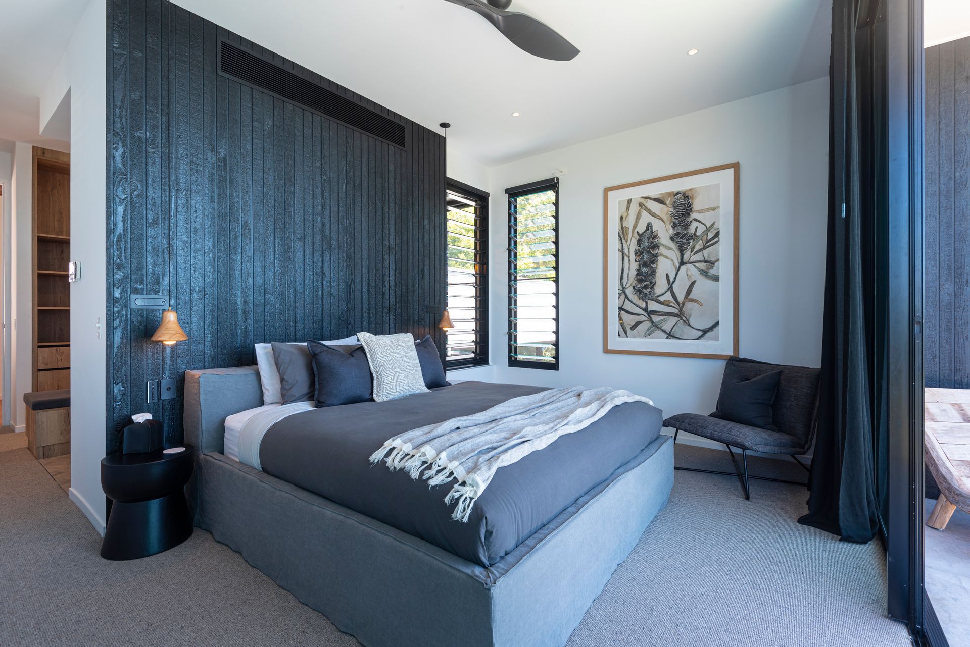 Modern Bedroom With Gray Bed, Dark Accent Wall, Art, and Large Windows — Red Emperor Constructions in Cannonvale, QLD