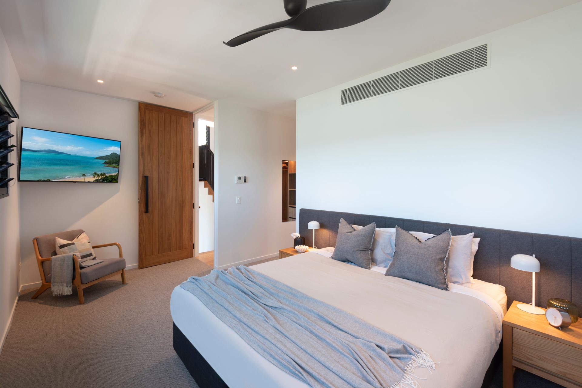 Bedroom With a Bed, Armchair, Wooden Door, and Tv — Red Emperor Constructions in Cannonvale, QLD