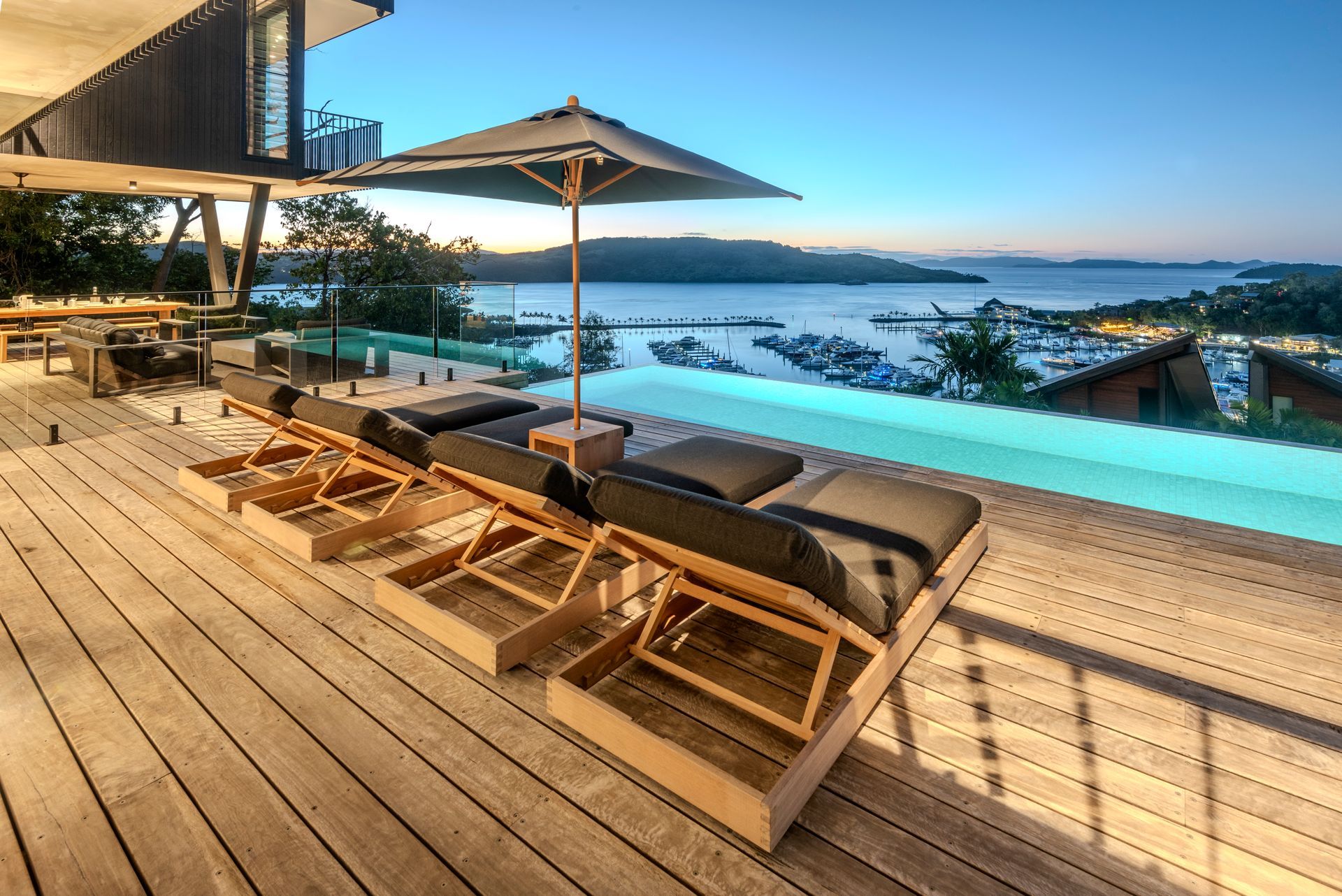 Wooden Deck With Pool and Lounge Chairs Overlooking a Harbor at Dusk — Red Emperor Constructions in Cannonvale, QLD