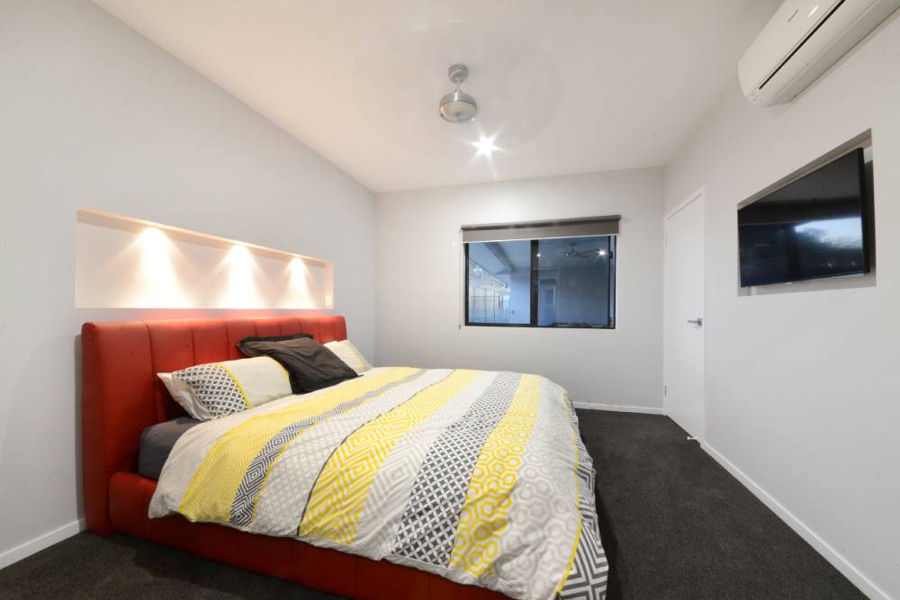 A bedroom with a large bed and a flat screen tv on the wall — Red Emperor Constructions in Cannonvale, QLD