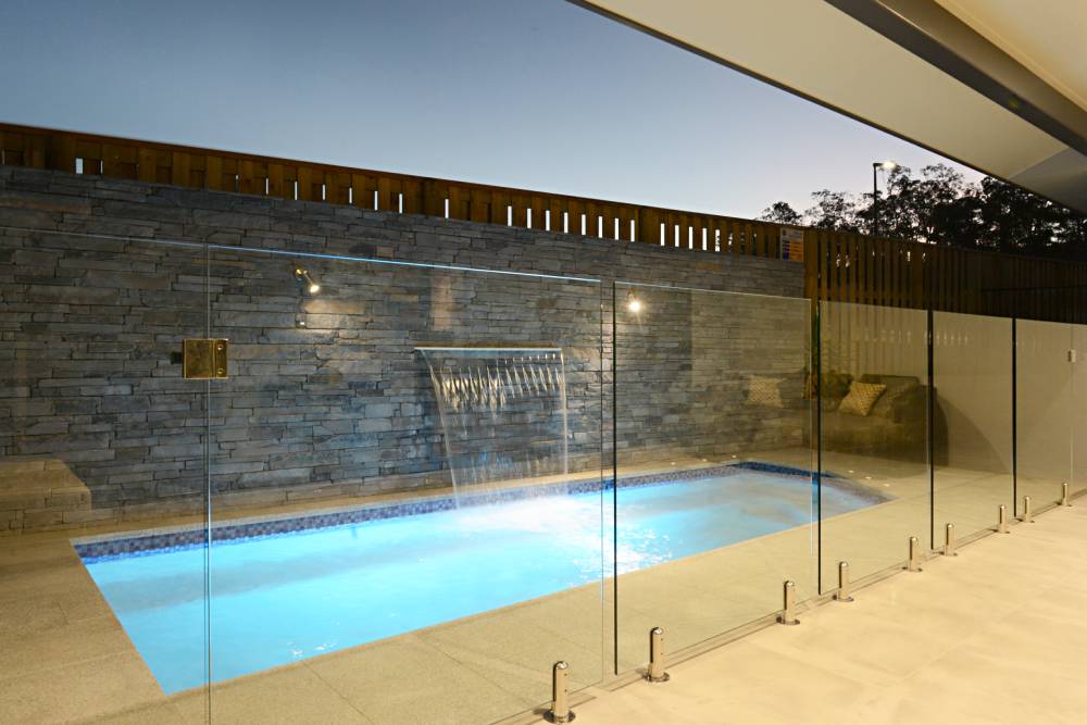A swimming pool with a waterfall behind a glass fence — Red Emperor Constructions in Cannonvale, QLD