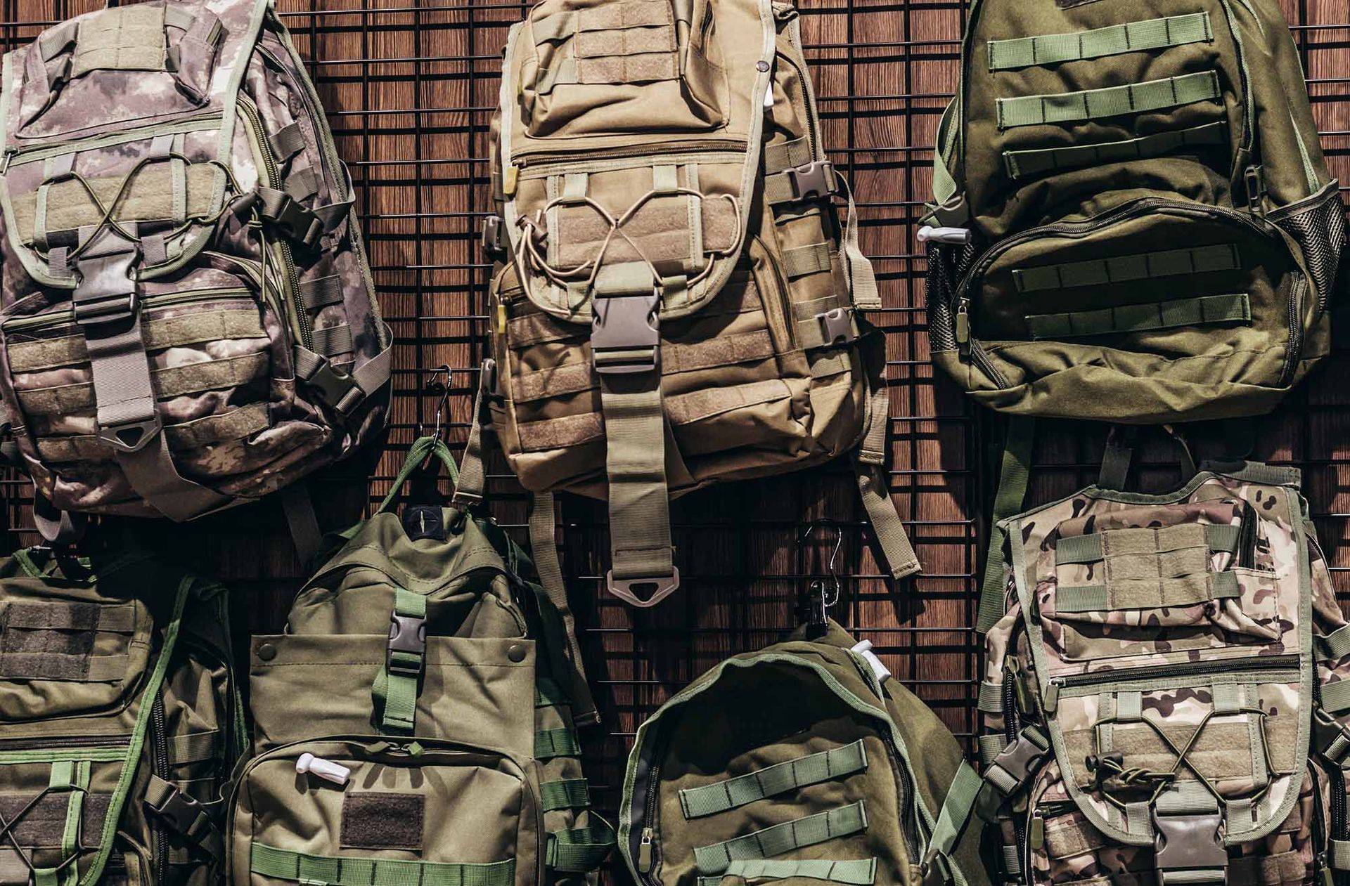 A bunch of tactical backpacks are hanging on a wall.