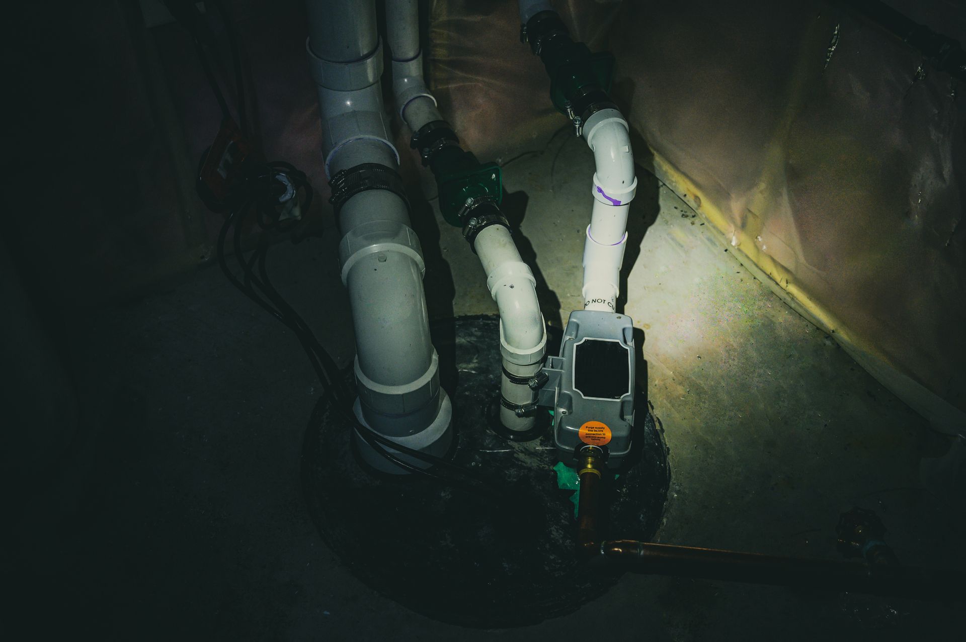 Industrial pipes and a pump in a dim, wet trench or sewer tunnel