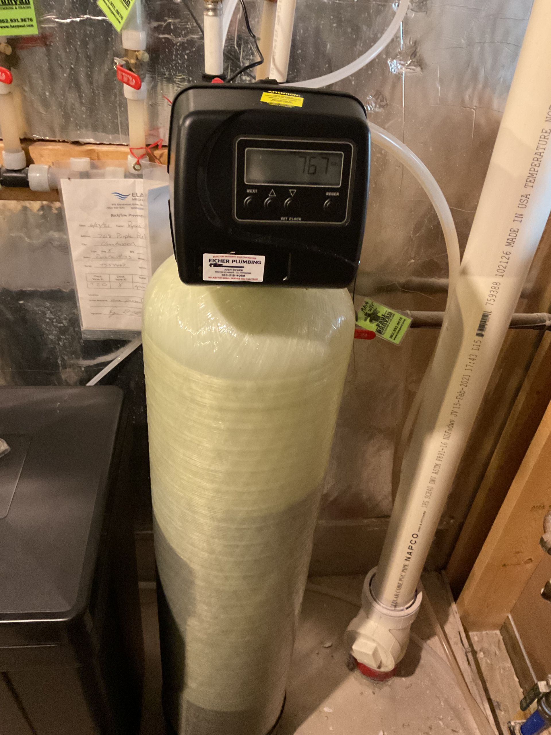 Water softener tank in a basement utility area with pipes and plumbing connections