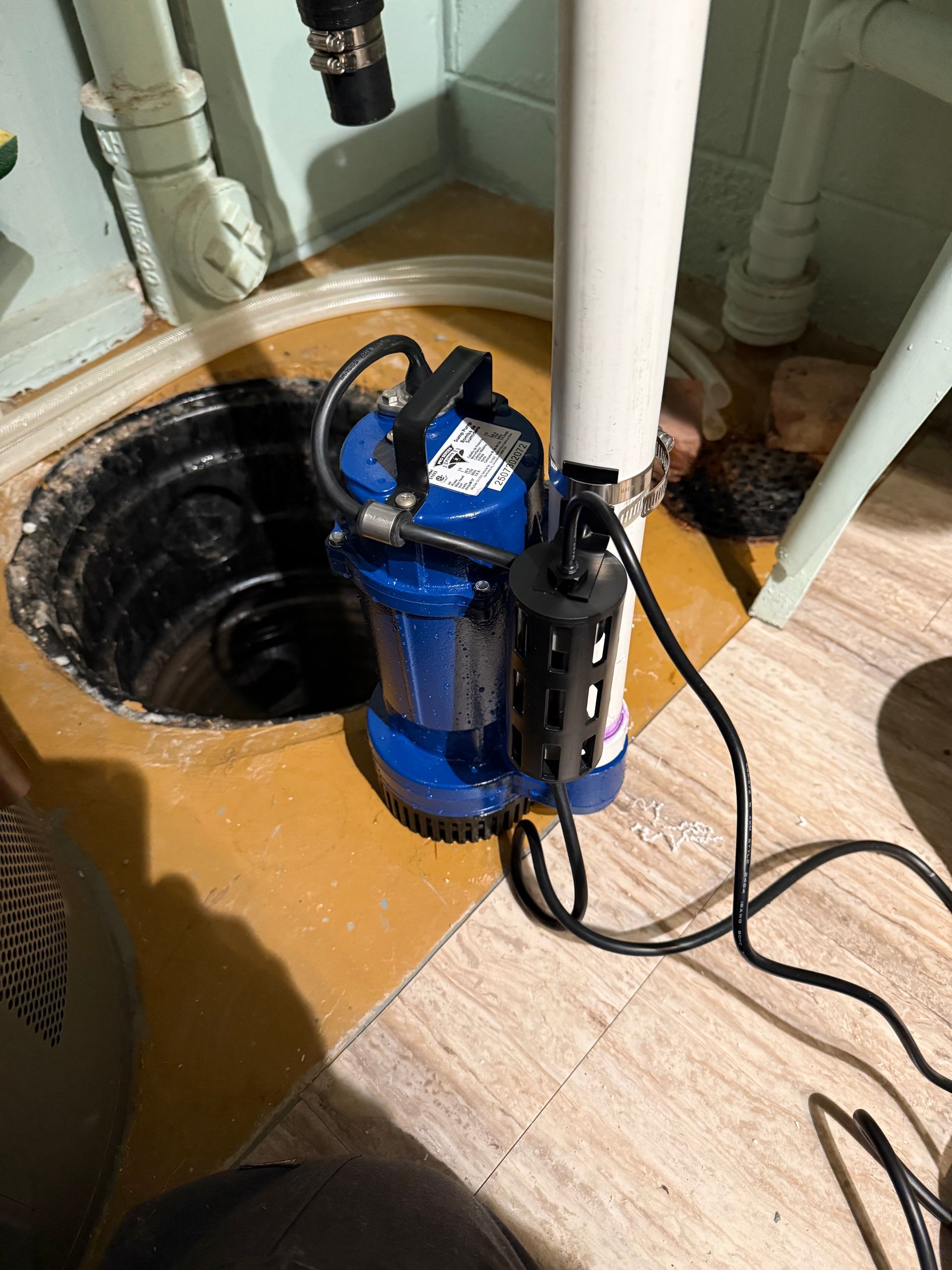 Blue submersible pump in a basement utility area beside an open floor drain.