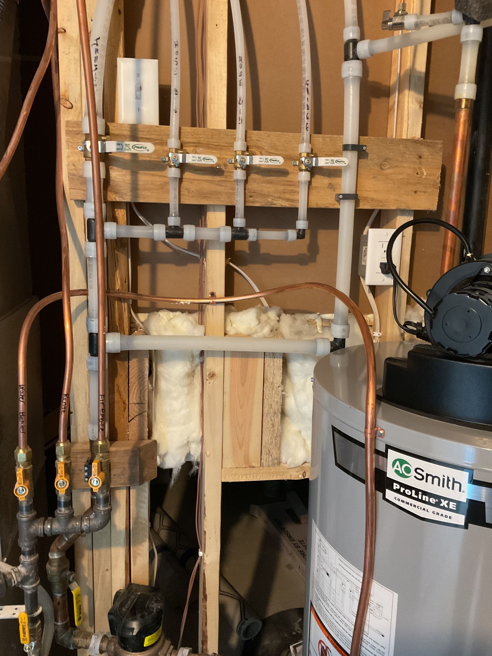 Plumbing pipes and valves beside a Smith water heater in an unfinished utility area