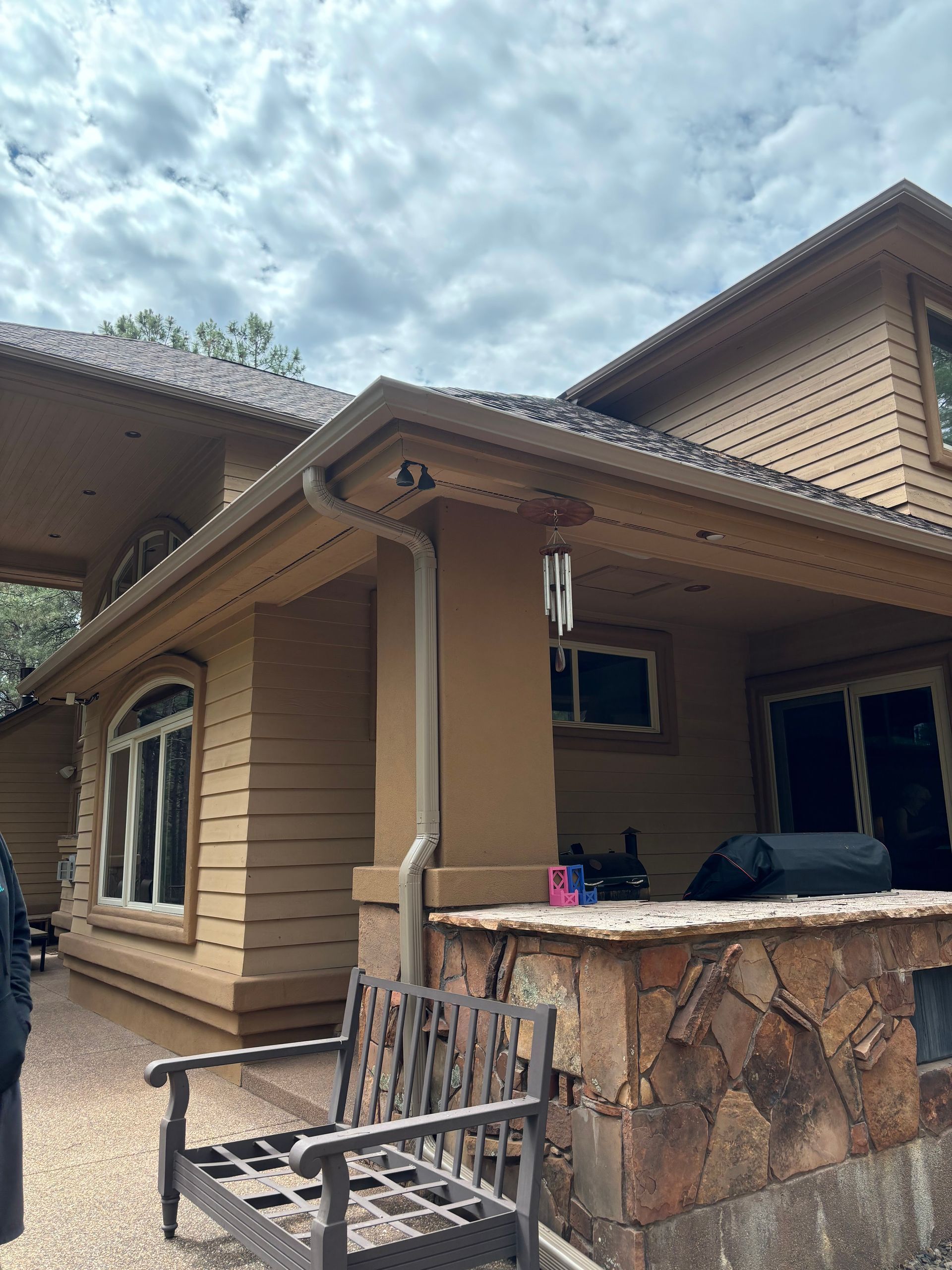 A tan house exterior with a stone-accented patio, a wooden bench, and a covered porch under a cloudy sky.